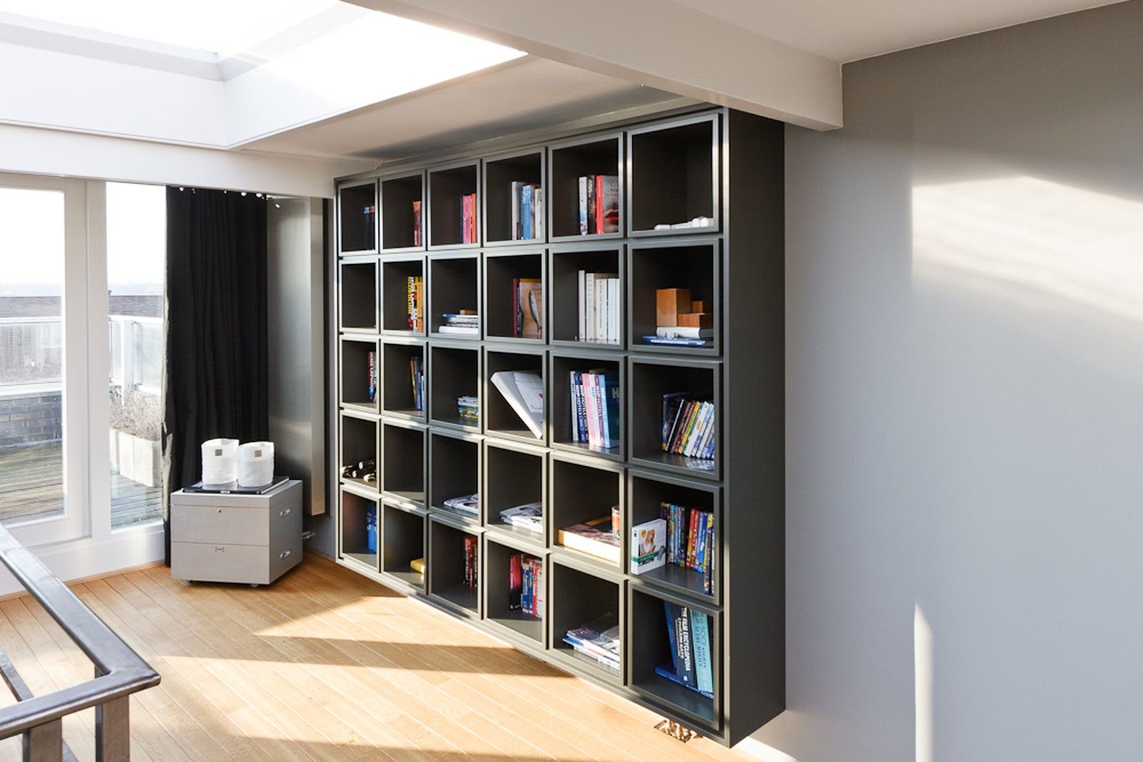 Zwevende vakkenkast met dertig compartimenten, deels gevuld met boeken.