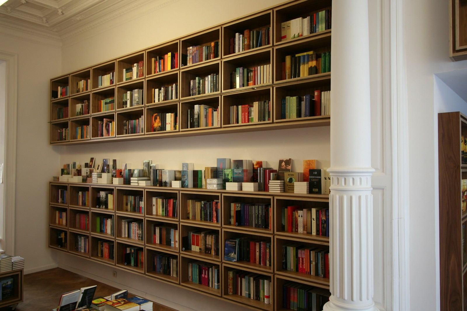 Wandvullende boekenkast met een dicht raster van vakken, in notenfineer.