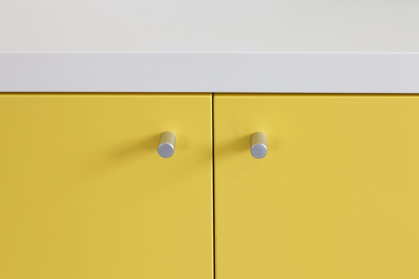 Twee aluminium knopjes op de gele deurfronten van het dressoir.