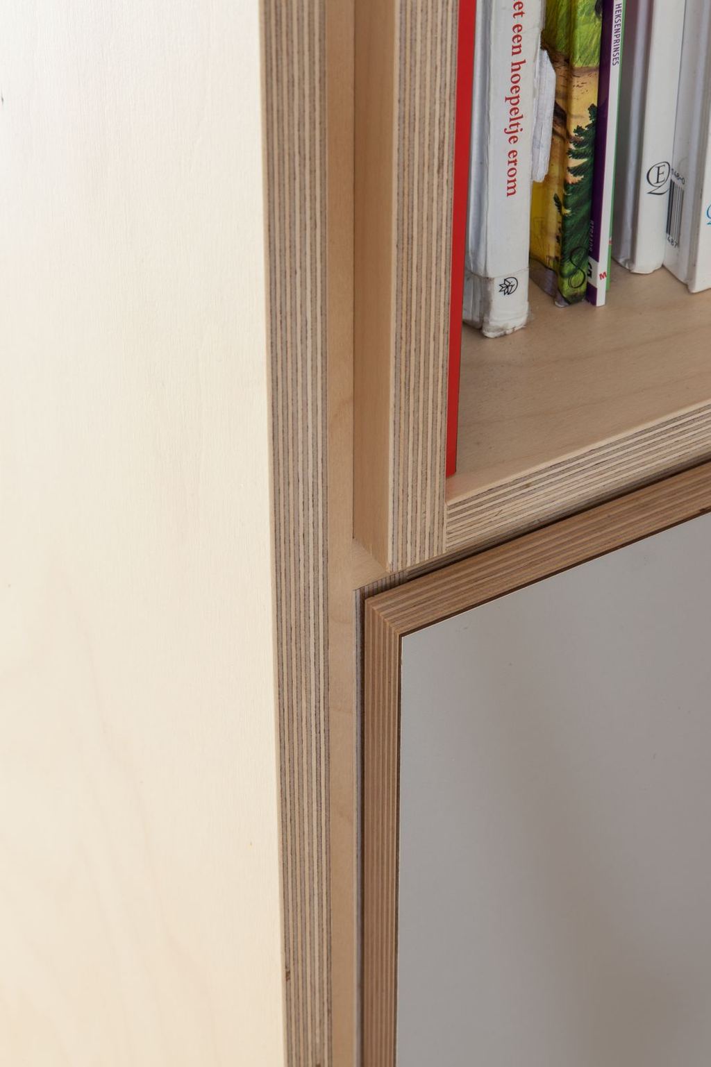 Boekenplank van berken multiplex naast een grijs kastfront.