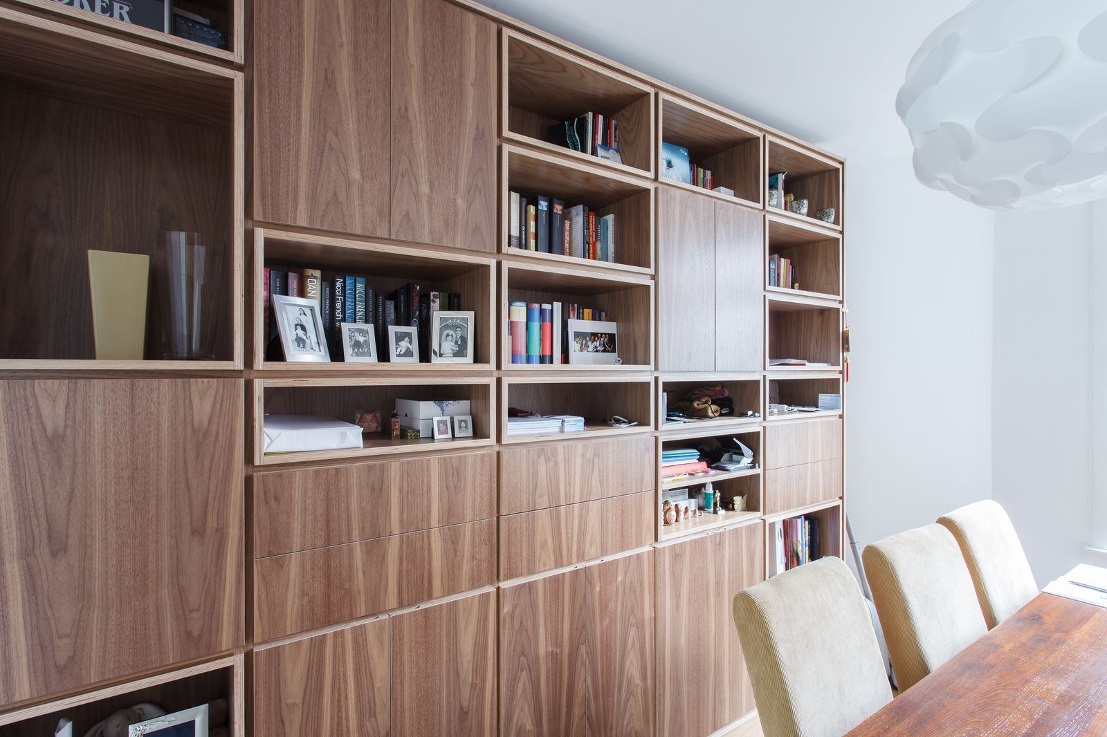 Notenhouten boekenkast met open en gesloten vakken vol boeken en foto's.