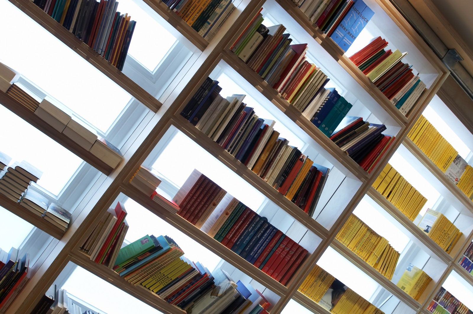 Wandvullende vakkenkast met boeken, van onderaf schuin gefotografeerd.