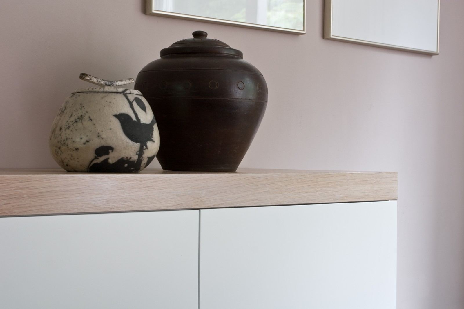 Zwevend dressoir met een licht houten bovenrand en witte deuren, met twee aardewerken potten erop.