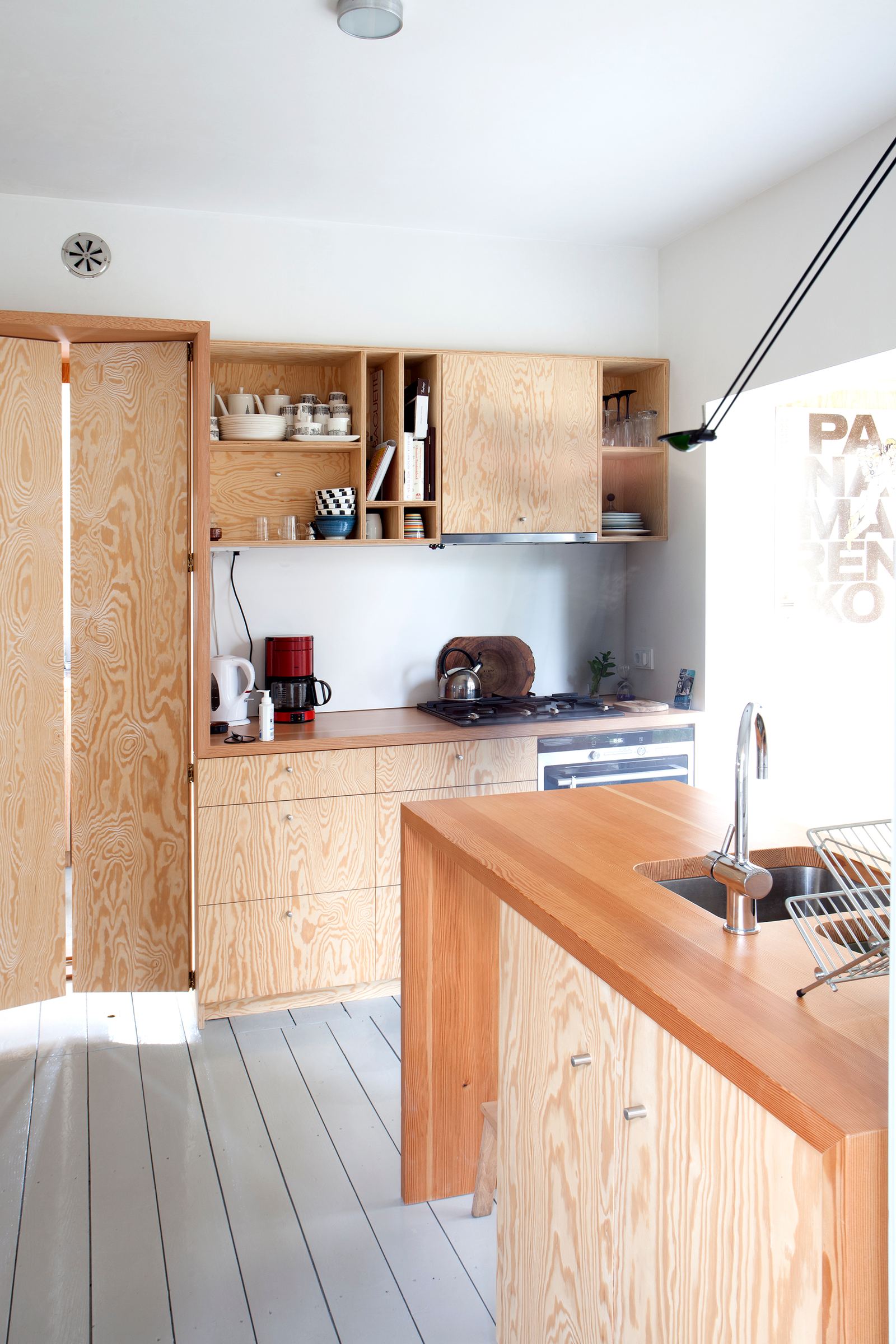 Houten keuken met een geopende vouwdeur, wandkasten en een hanglamp boven het eiland.
