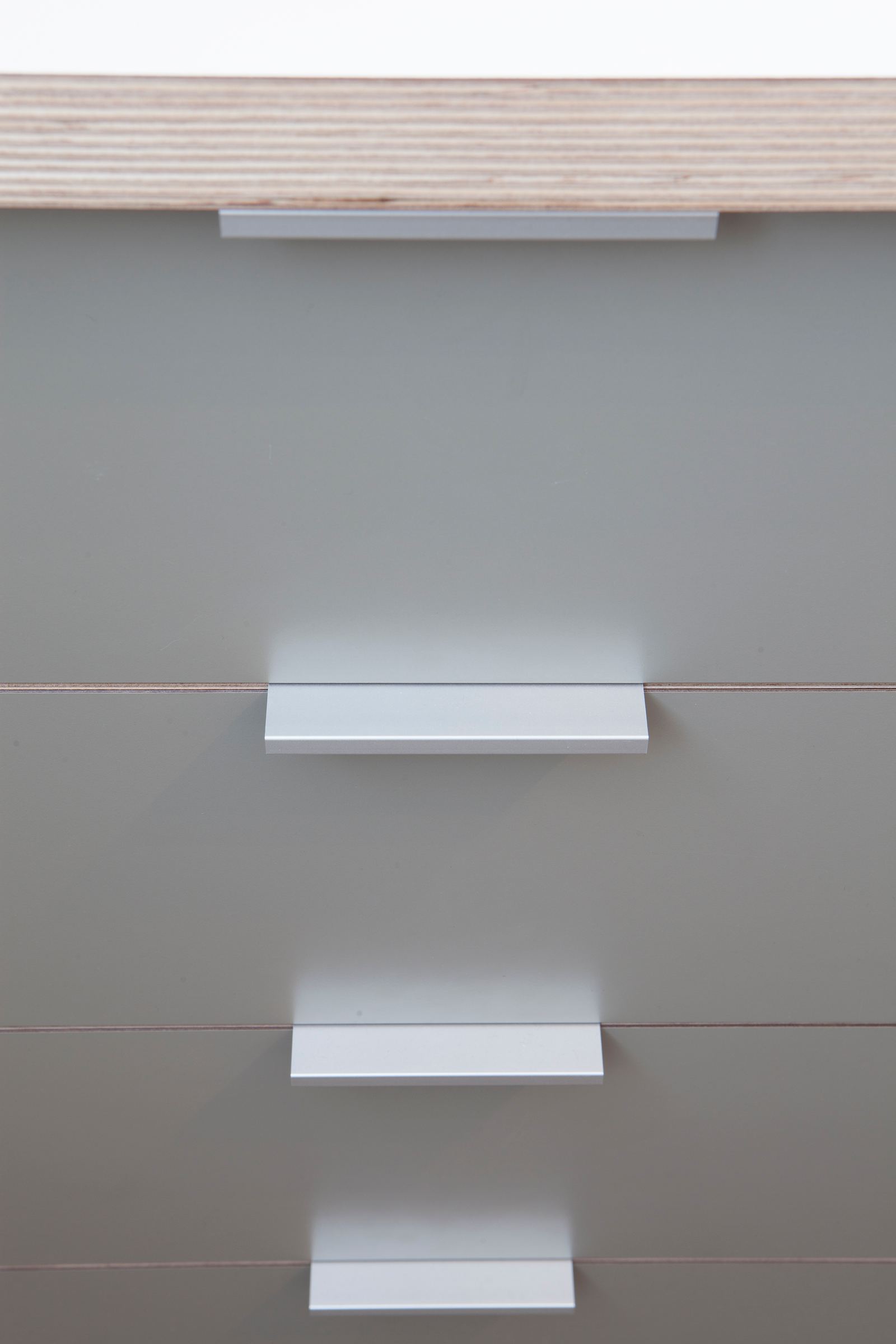 Detail van drie aluminium greeplijsten op grijze ladefronten.