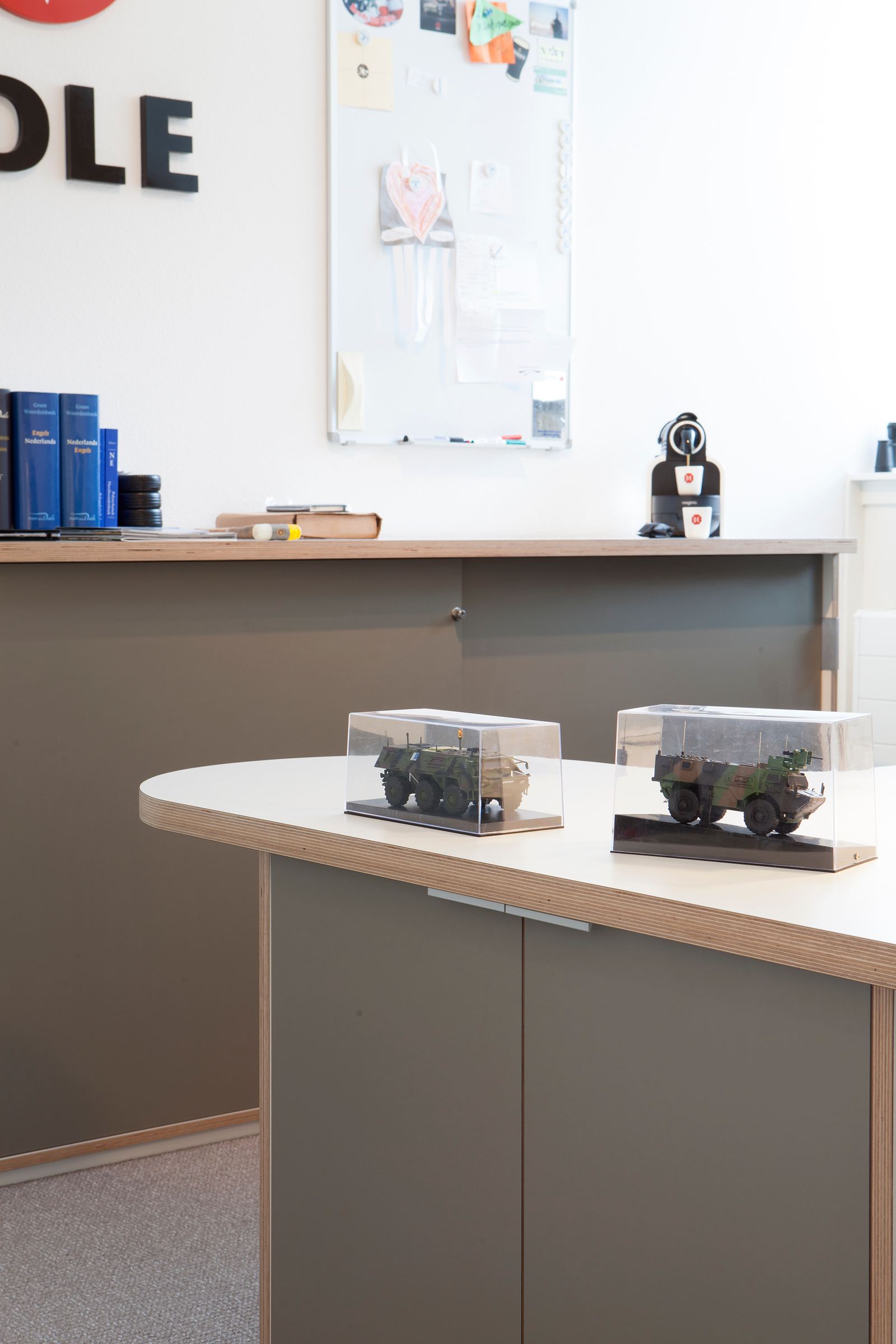 Nierkast-vormig bureaublad met plaatrand, met twee modelvoertuigen in vitrines erop.